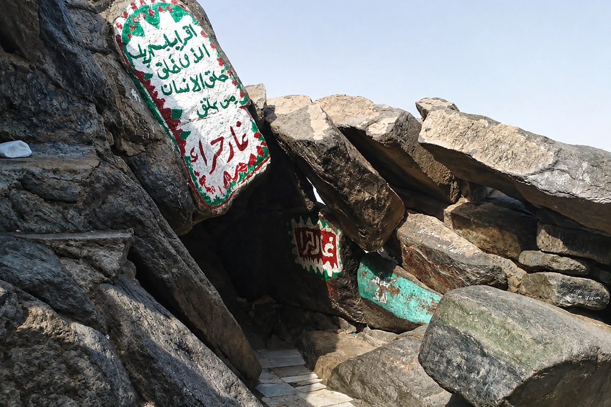 The narrow rock entrance to the Cave of Hira near the summit of Jabal al-Noor, worn boulders and bare stone around it, with the Makkah valley falling away in the haze below.