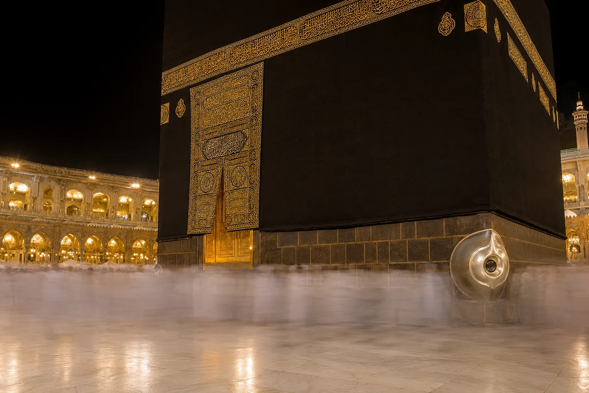 The eastern wall of the Kaaba in Masjid al-Haram, showing the raised gold door and the silver-framed corner of the Black Stone, with the stretch of Kiswah-draped wall between them.