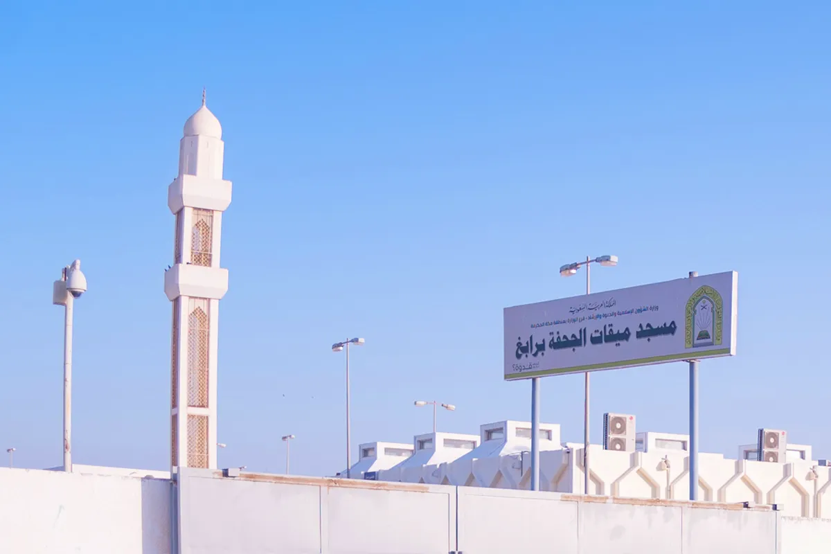 A large modern miqat mosque beside the coastal highway at Rabigh, wide white arcades and a broad car park, flat scrub country and the Red Sea haze in the distance.