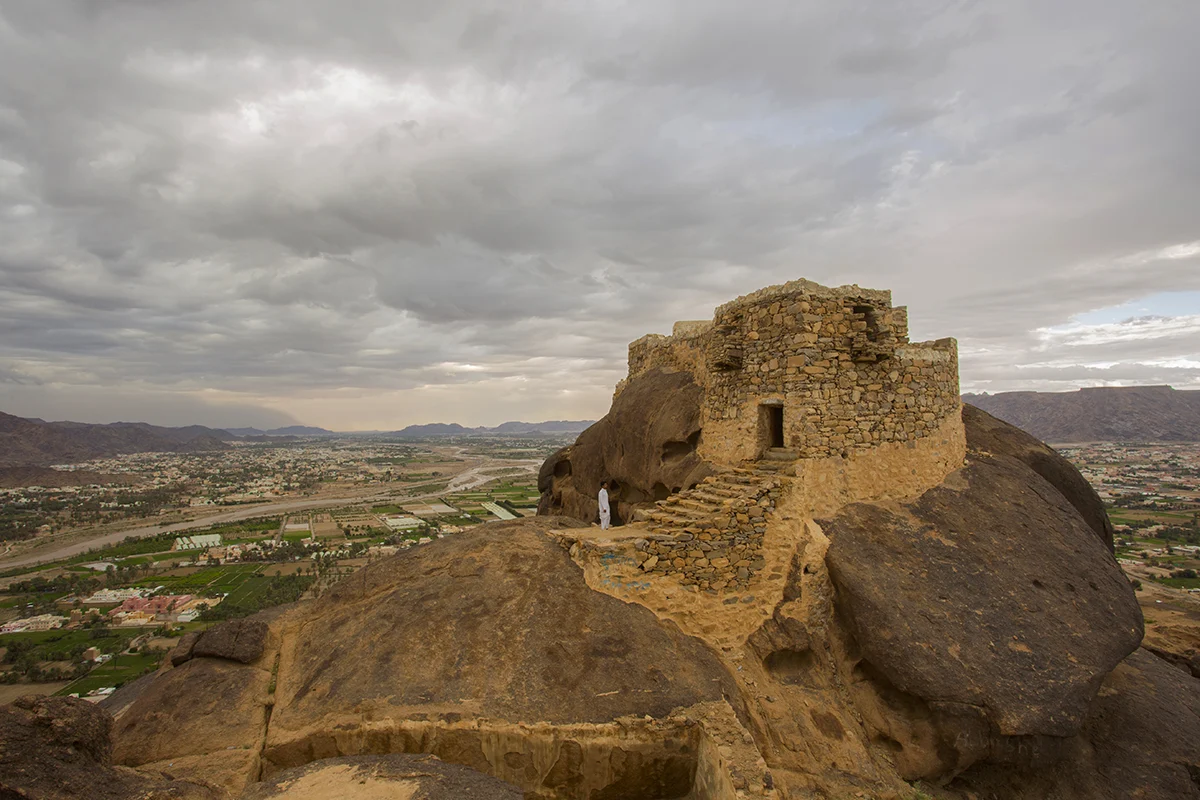 The stone foundations and mud-brick wall lines of the ancient walled city at al-Ukhdud in Najran, spread across open ground under clear daylight.
