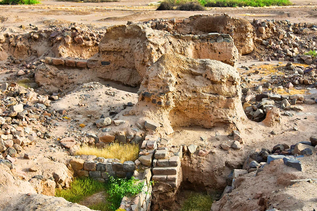 A long shallow trench cut in bare stony ground at the al-Ukhdud site in Najran, empty and unmarked, under flat daylight.