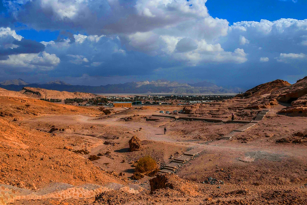 Sandstone cliffs with rock-cut tomb facades above the palm oasis of al-Bad' in Tabuk Province, weathered and unrestored, in warm late light.