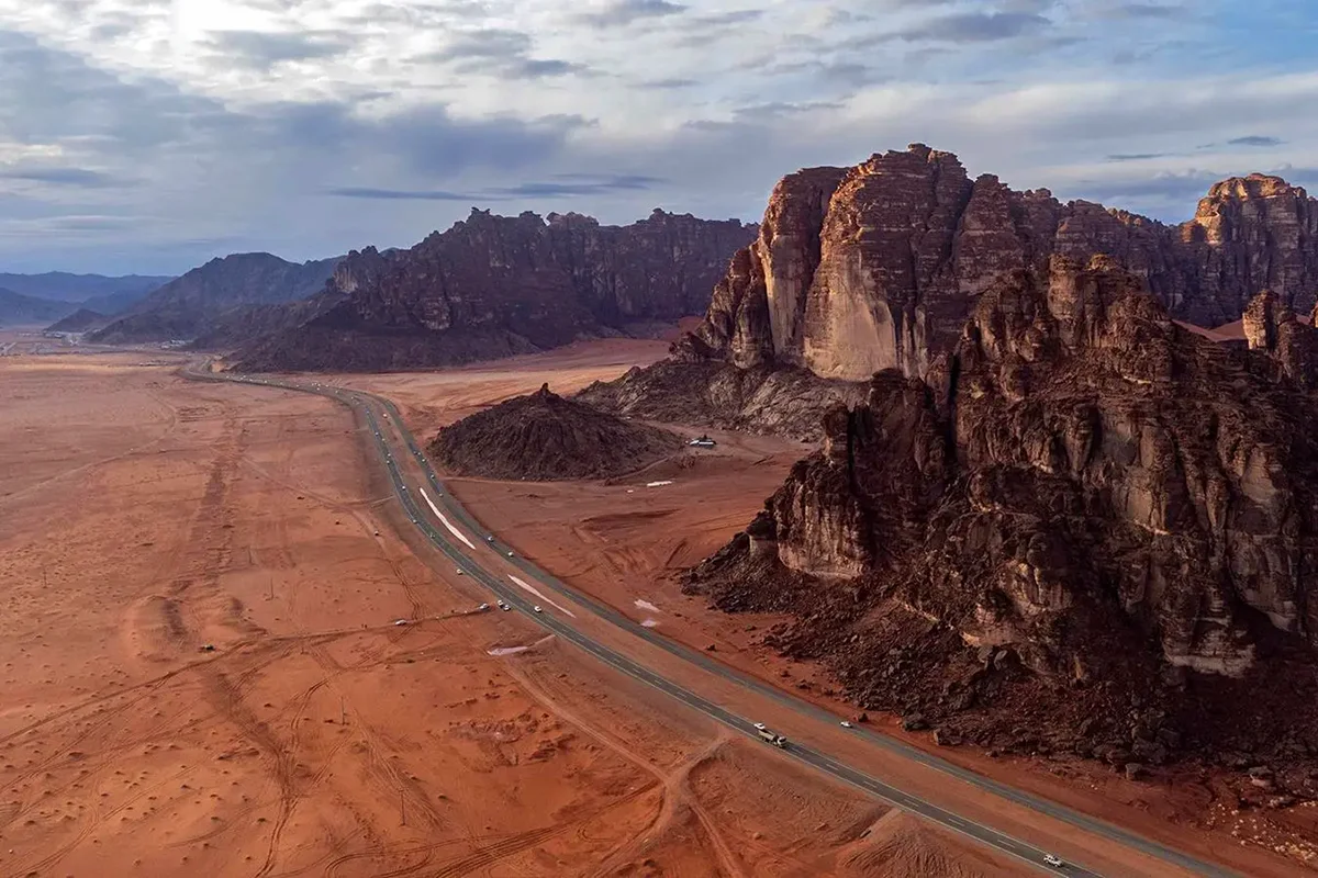 Open gravel plain and low bare hills in the Tabuk region under hard midday light, empty and dry, with the horizon flat and distant.