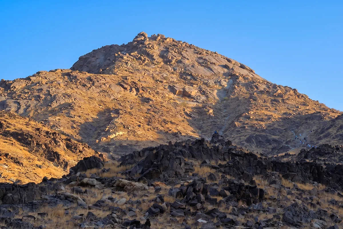 The bare rocky summit of Jabal Thawr rising south of Makkah in early morning light, its lower slopes gentle and its upper crags broken and steep, with the city haze low behind it.