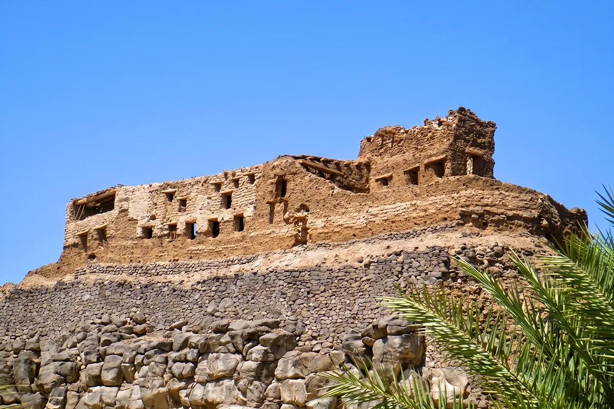 Weathered stone fortification remains of uncertain date on a rocky rise at Khaybar, with the black lava field and palm oasis in the distance.