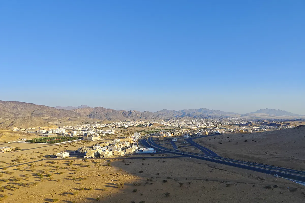 An empty desert road running south-west from Madinah between low brown ridges towards Badr, with open gravel country on both sides in early morning light.
