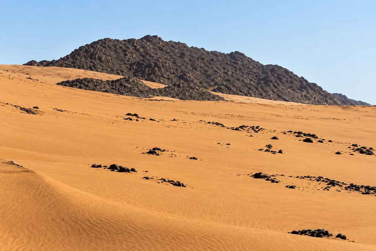 The far ridge at Badr seen from across the valley floor, a long sandy shoulder rising above open gravel ground with bare hills behind it.