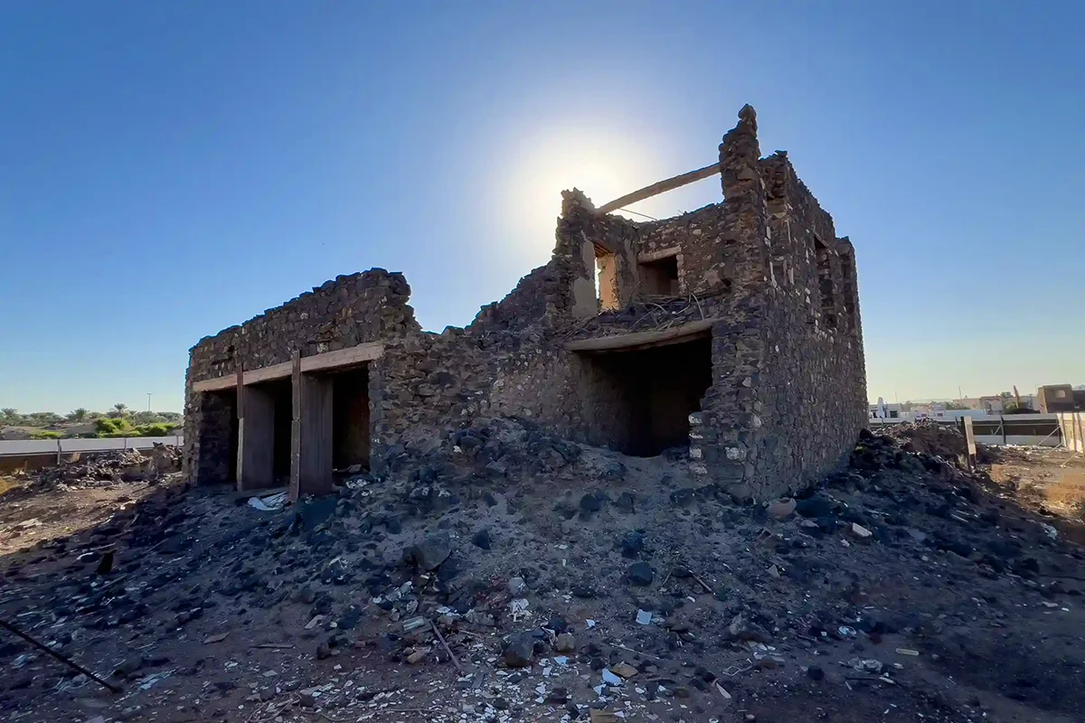 A dry stone-lined well shaft partly filled with sand and rubble in open ground outside Madinah, unmarked and unremarkable, in flat daylight.
