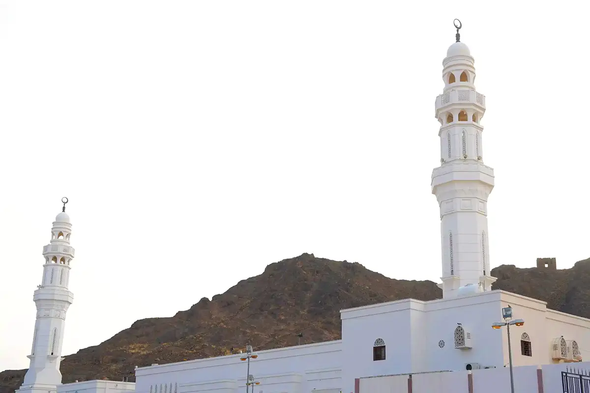 Open stony ground and low modern buildings on the eastern edge of Madinah towards the Awali, with bare brown hills in the distance under afternoon light.