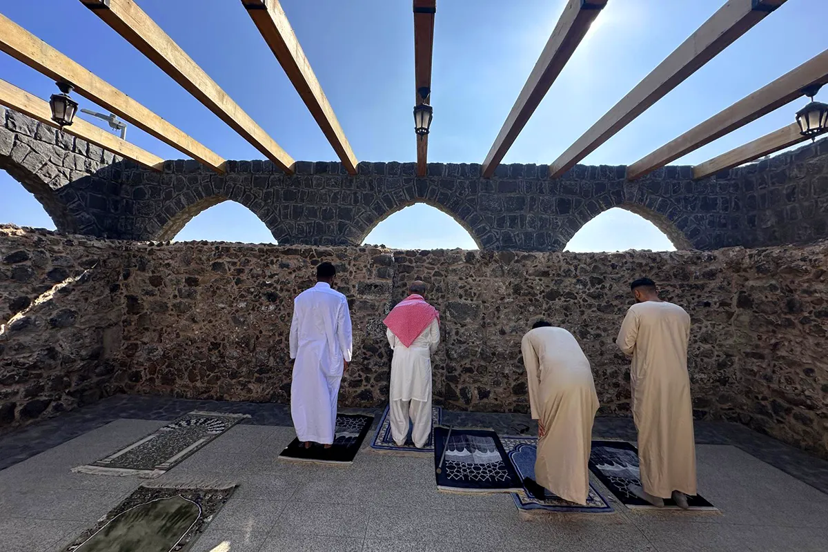 A small plain cream stone neighbourhood mosque with a low dome and short minaret on a quiet residential street in Madinah, in warm afternoon light.