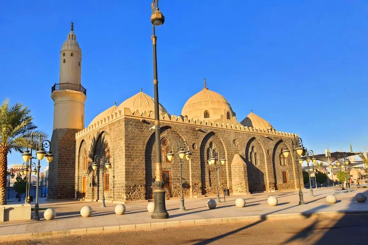 The pale stone exterior of Masjid al-Ghamamah in Madinah with its row of low Ottoman domes, seen from the street in warm late afternoon light.