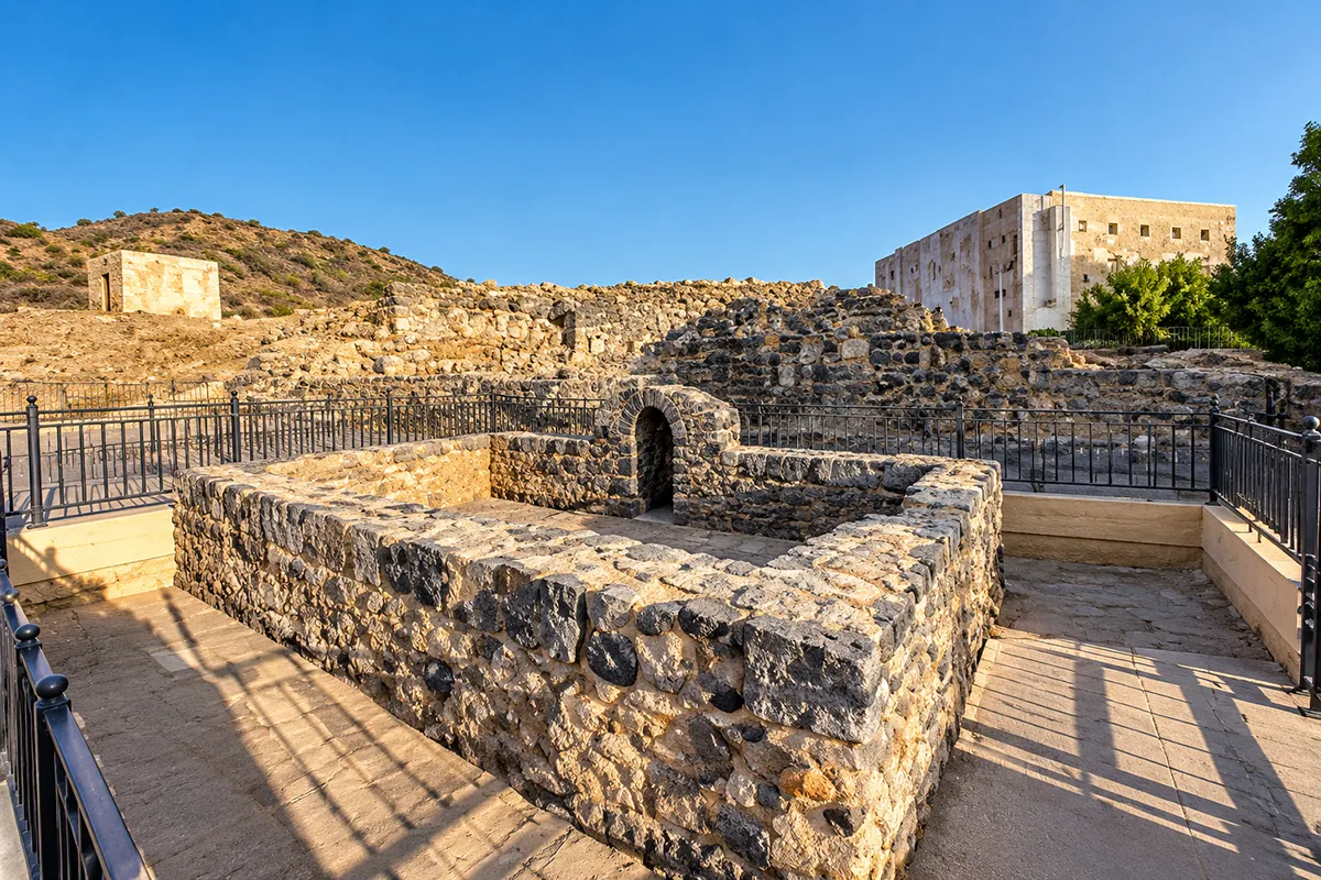 A low unroofed rectangular walled plot on the rocky slope at the Seven Mosques site in Madinah, open to the sky, with Mount Sela' rising behind it.