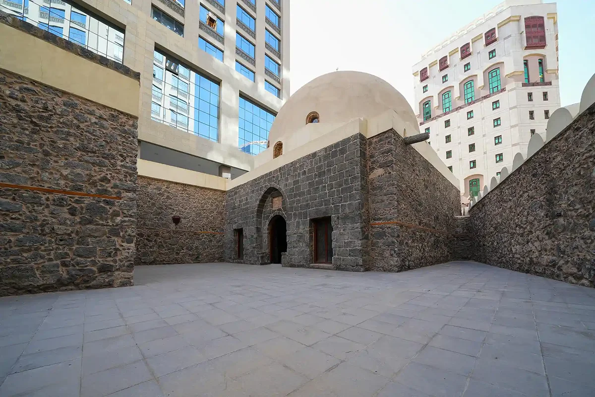A small plain whitewashed historic mosque raised on the rocky slope of Mount Sela' in Madinah, with an open forecourt in front and bare rock rising behind.