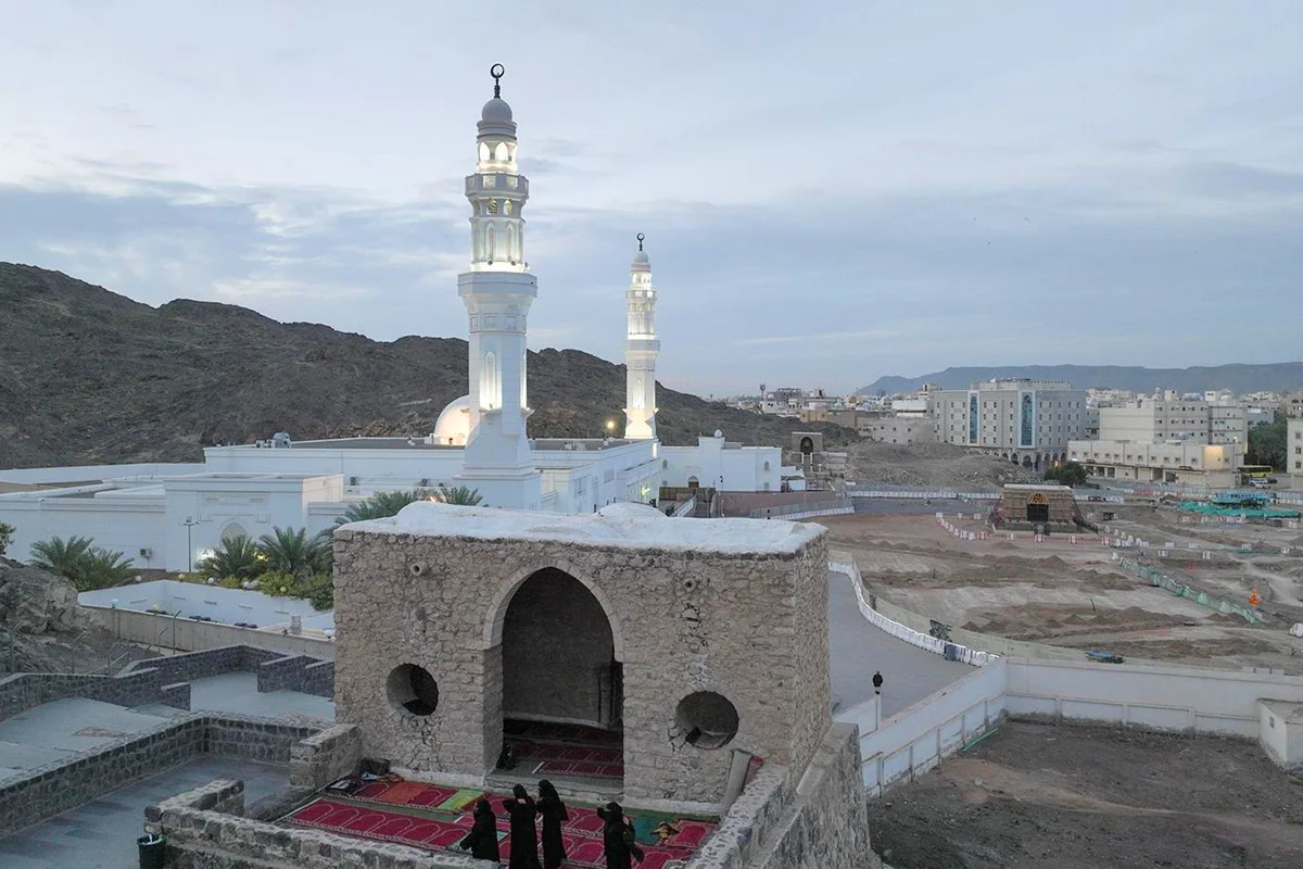 The small whitewashed Masjid al-Fath standing on raised rocky ground at the foot of Mount Sela' in Madinah, with its low dome and short minaret in warm late afternoon light.