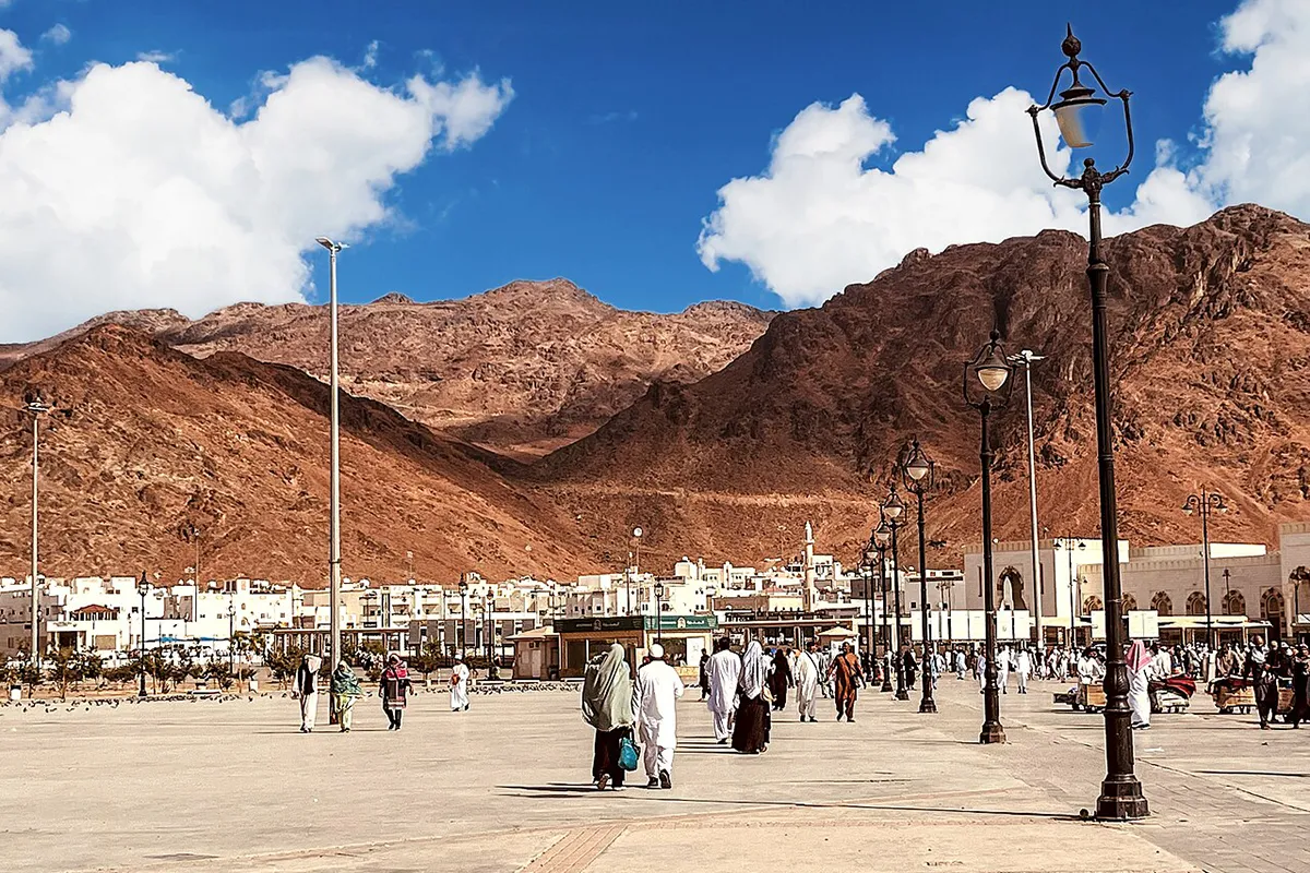 The flat gravel plain of the Uhud battlefield seen from the slope of the archers' hill, with the long red ridge of Mount Uhud filling the background under clear morning light.