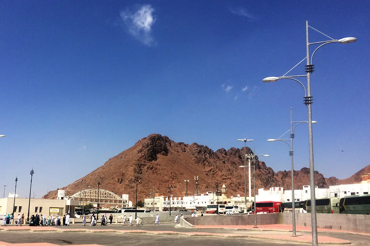 The low rounded rise of Jabal al-Rumah, the Archers' Hill, standing alone on the flat gravel plain at Uhud with the red mass of the mountain behind it in early morning light.