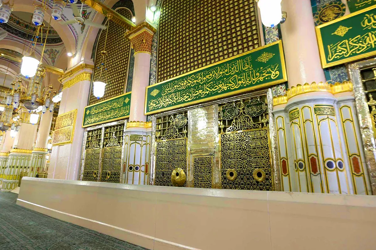 The exterior wall and ornate metal grille screen of the Prophet's chamber inside Masjid an-Nabawi, lit by warm even mosque lighting, with no people in focus.