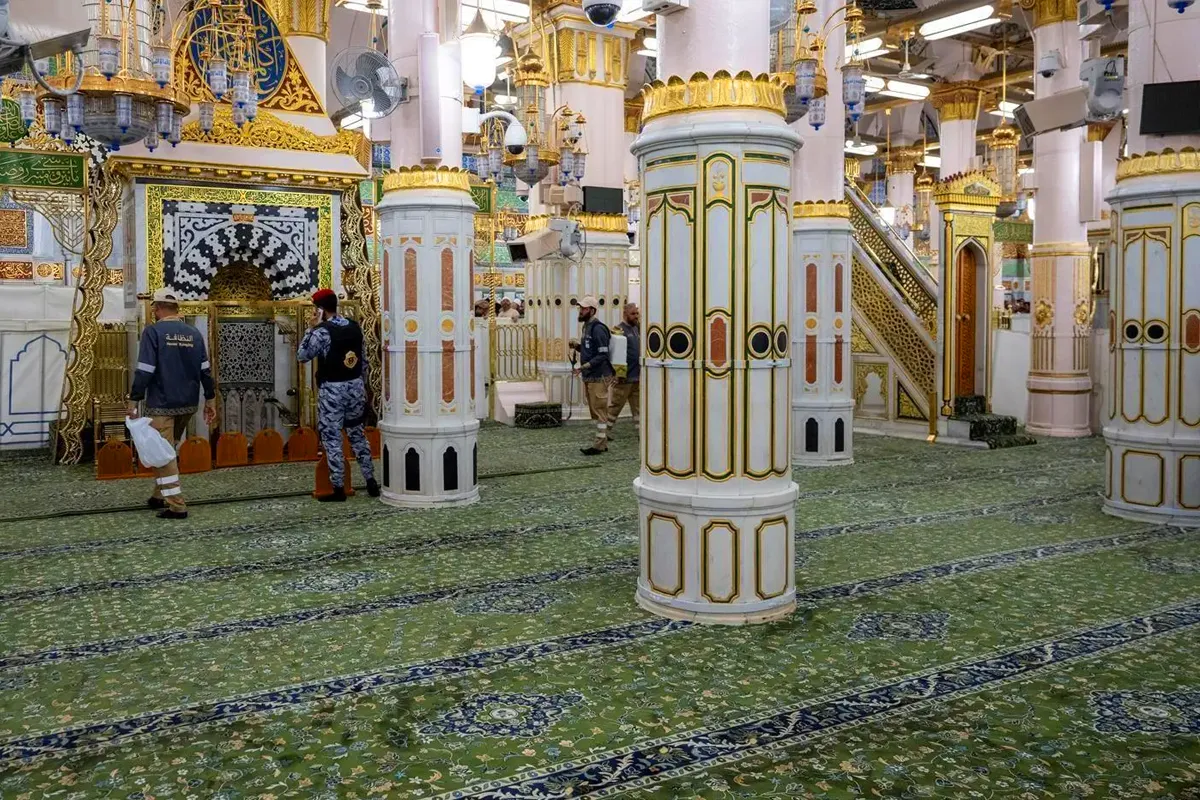 The interior of the old prayer hall of Masjid an-Nabawi near the Rawdah, showing pale historic columns, patterned arches and carpeted floor in warm even mosque light, with no faces visible.