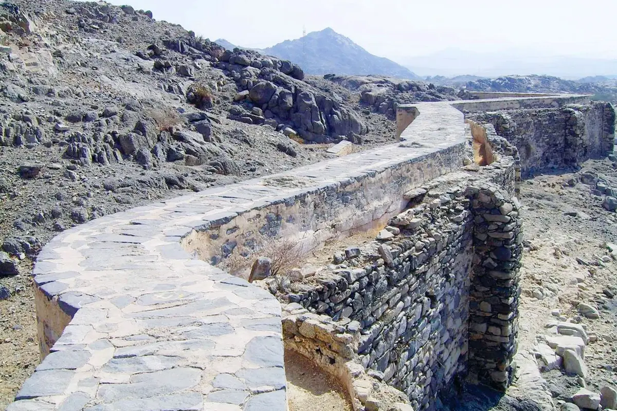 A weathered stone and plaster aqueduct arch of the Ayn Zubaydah channel standing about ten metres high on dry ground between Arafat and Muzdalifah in morning light.
