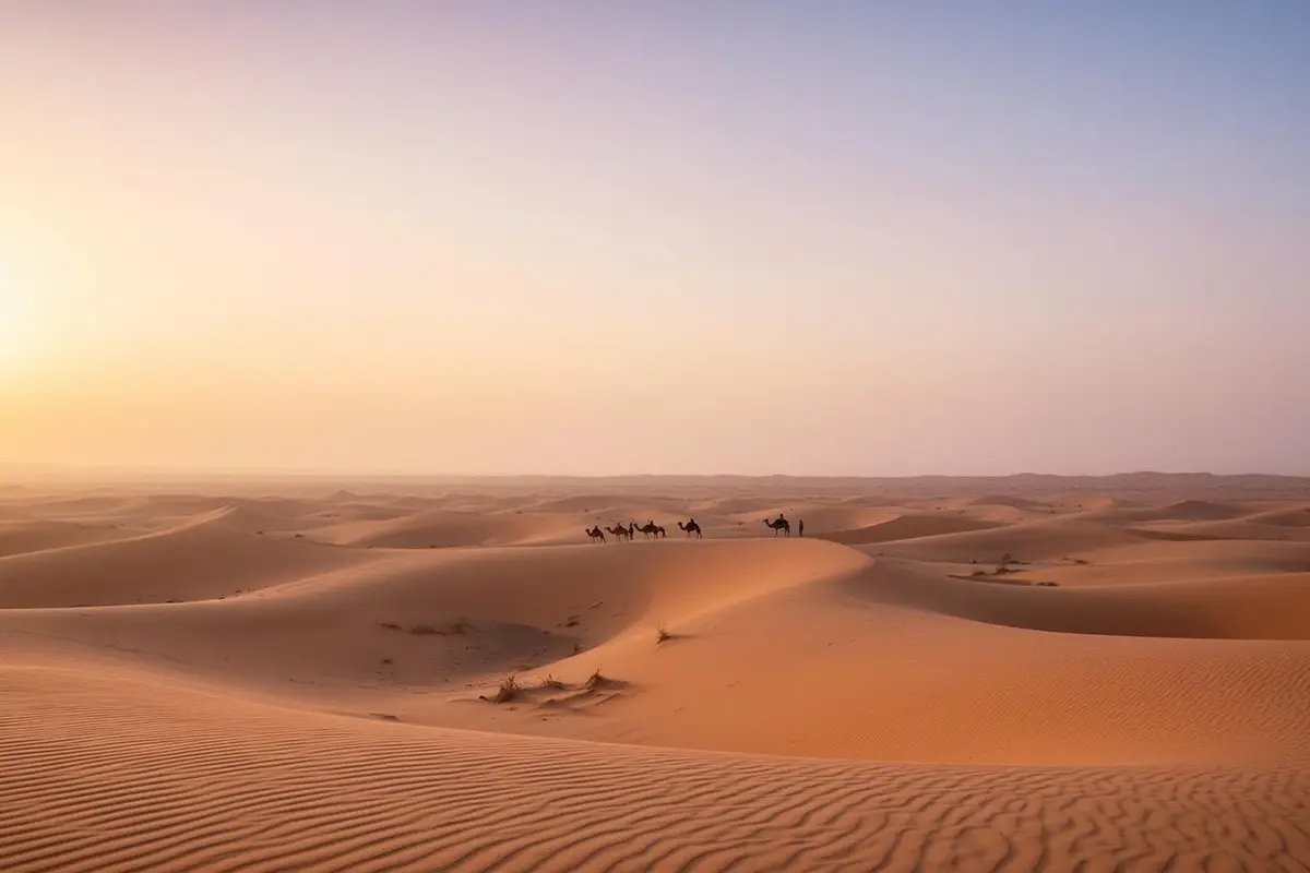 A long empty desert track running north between low dark ridges on the old road between Makkah and Madinah, dry gravel plain and heat haze on a distant line of hills.