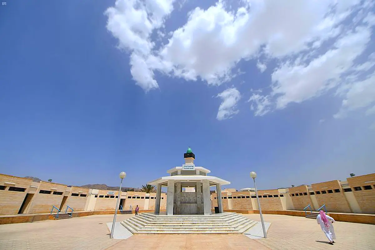 The miqat mosque at Wadi Muharram high on the al-Hada escarpment above Taif, white walls and a slim minaret against a steep drop, cloud lying below in the valley.