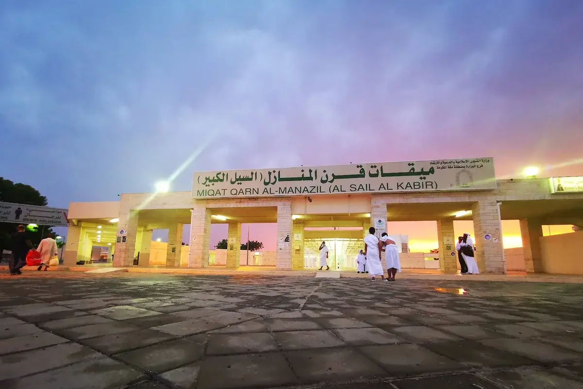 The large modern miqat mosque at al-Sayl al-Kabir on the Makkah to Taif highway, wide white arcades and a broad car park, bare brown hills rising behind it under a hard midday sky.