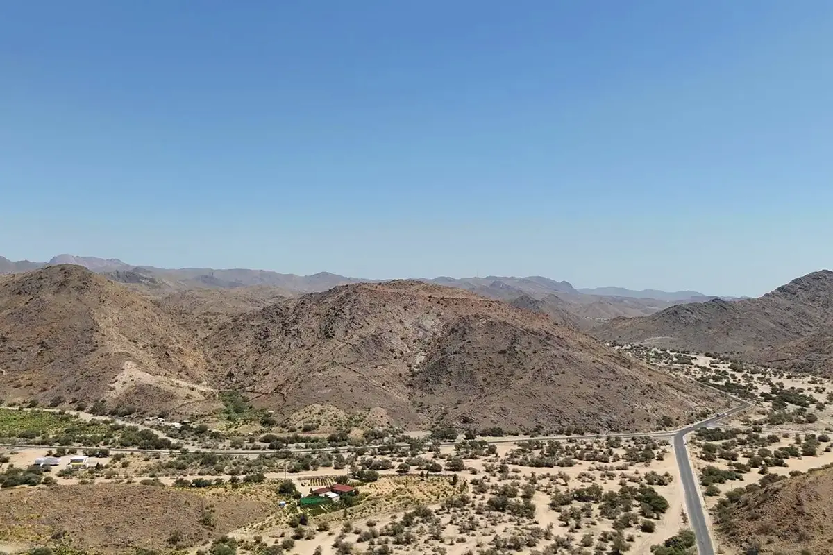 Open high ground east of Taif in flat afternoon light, dry grazing country running to distant blue ridges, scattered thorn trees and no buildings in sight.