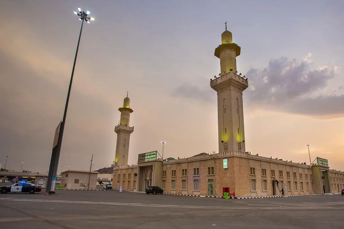 The long low rectangular Masjid al-Mash'ar al-Haram standing alone on the open ground of Muzdalifah at dawn, plain walls and a single minaret, empty stony ground stretching away on all sides.