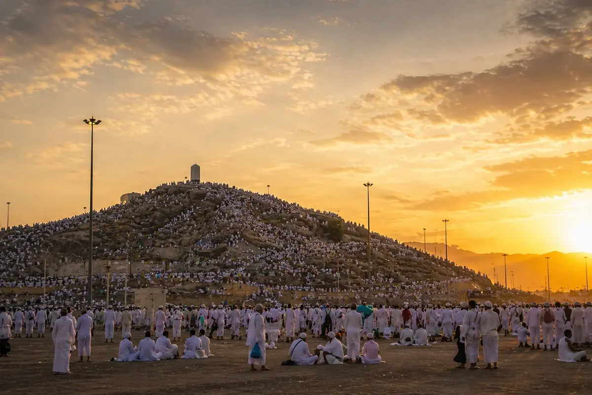 The wide flat plain of Arafat ringed by a semicircle of low brown mountains, the small rocky rise of Jabal al-Rahmah with its white pillar in the middle distance, dry gravel ground stretching to the horizon.