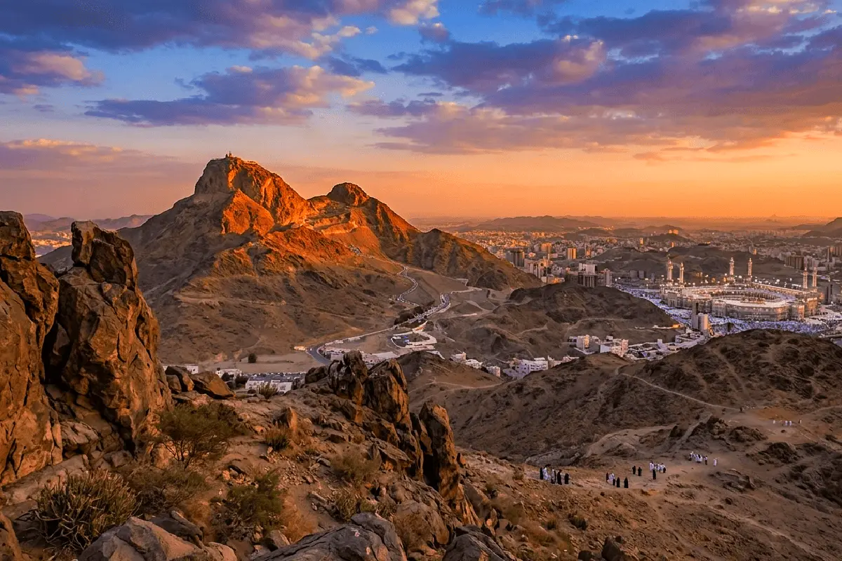 The narrow rocky defile at Aqaba on the Makkah edge of Mina at night, bare stone slopes closing in on both sides, modern Hajj lighting glowing faintly beyond the ridge.
