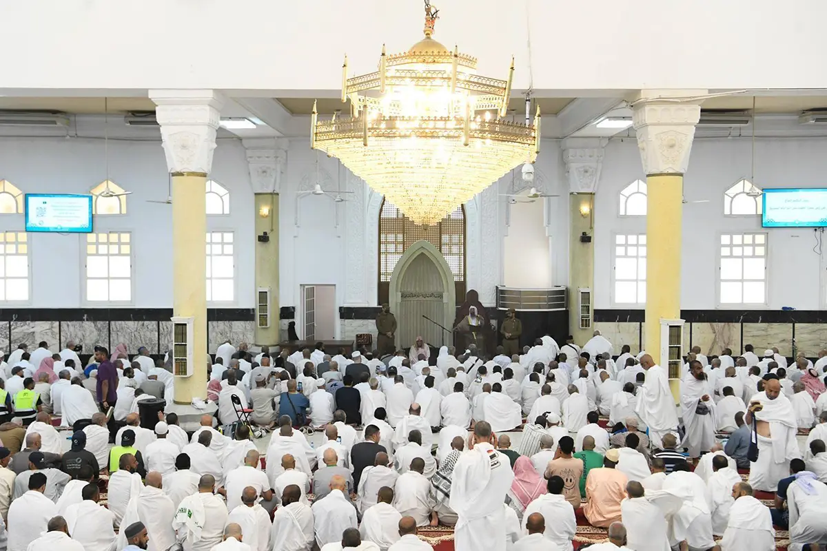 The wide low white mass of Masjid al-Khayf on the southern side of the Mina valley, four slim minarets rising from its courtyards, bare brown mountain slopes directly behind it.