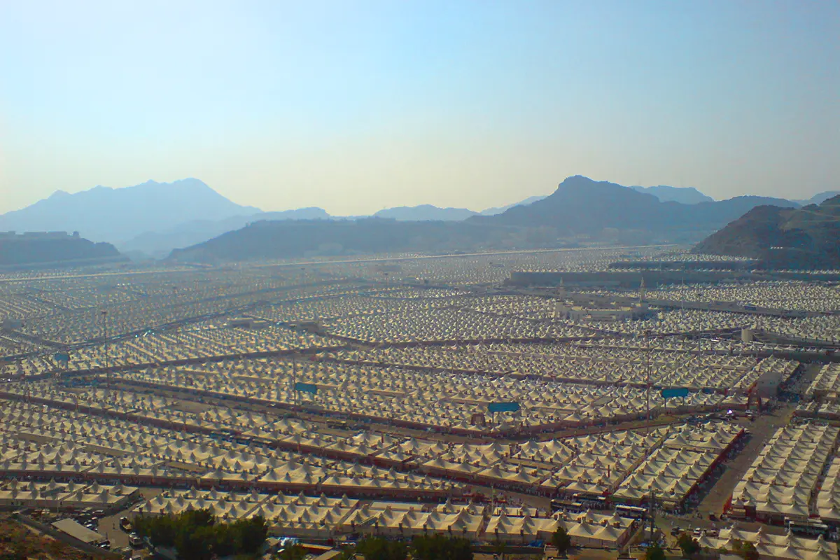The white tent city of Mina filling the valley floor between bare brown mountains east of Makkah, rows of air-conditioned tents in ordered blocks with roads running between them and the Jamarat complex in the distance.