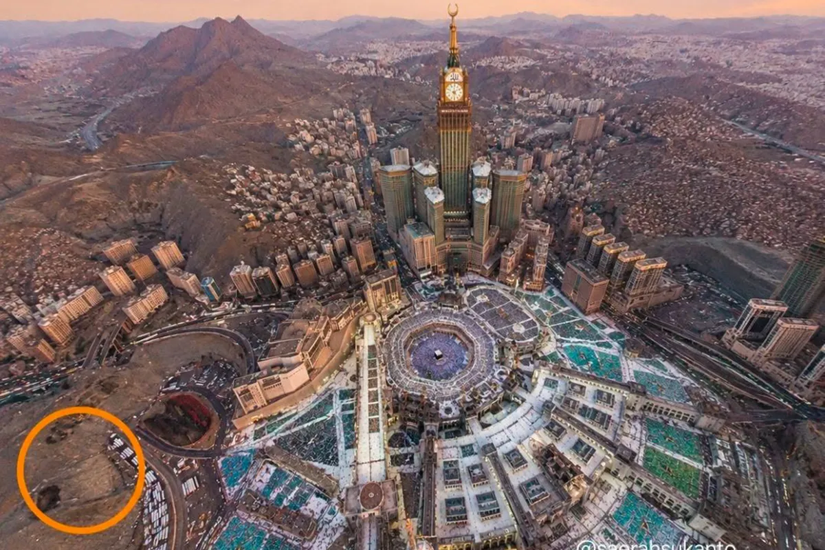 A narrow rocky valley on the eastern side of Makkah between steep bare hills, now filled with modern apartment blocks and a road, the old ravine shape still readable between the slopes.