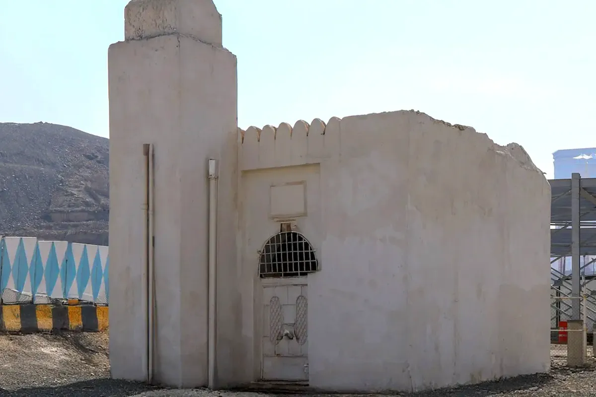 The low stone structure covering Bir Tuwa in the Jarwal district of Makkah, a protective wall around it, modern apartment blocks and a ring road flyover rising close behind.